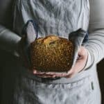 person in apron holding loaf of banana bread