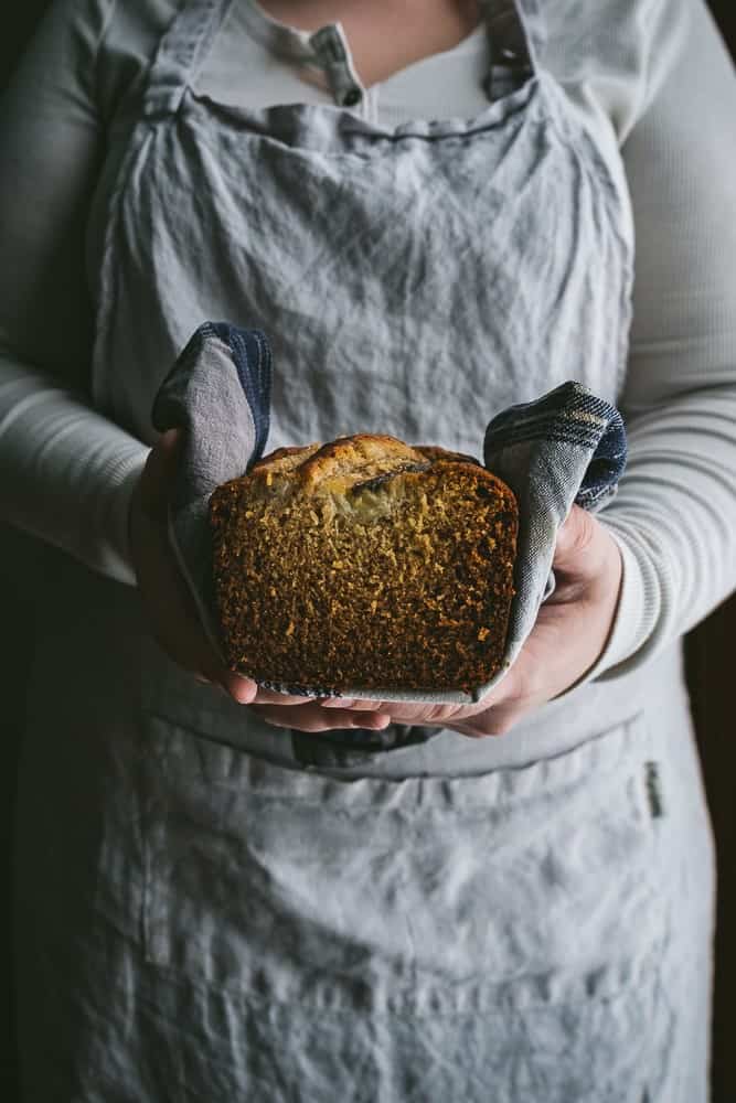 person in apron holding loaf of banana bread