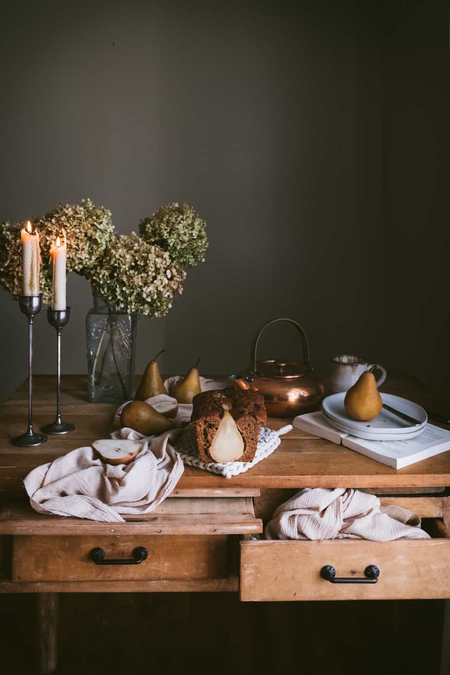 table with candles, dried hydrangeas, ginger pear loaf and copper pot