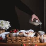 woman pouring milk into cup next to tray of muffins and strawberries