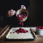 woman pouring cherries from a bowl onto a pie crust