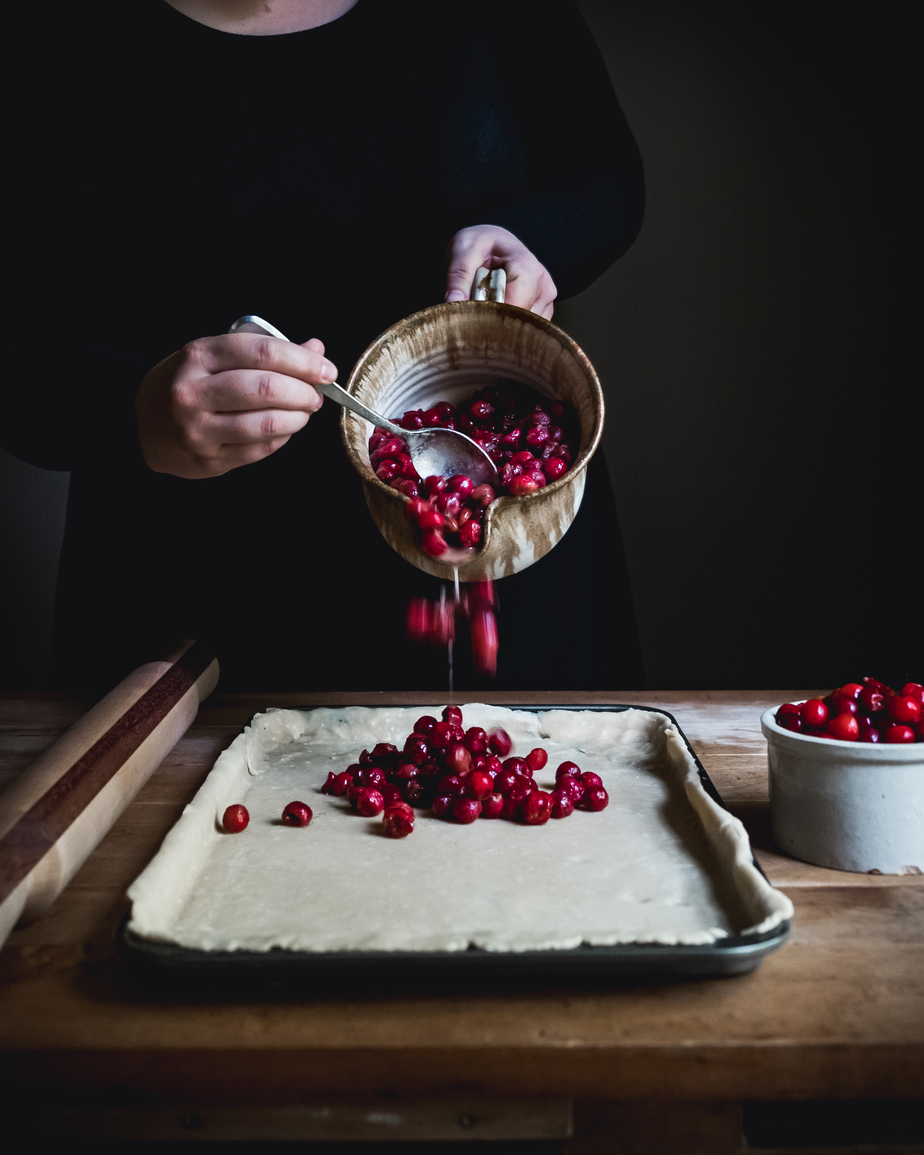 woman pouring cherries from a bowl onto a pie crust