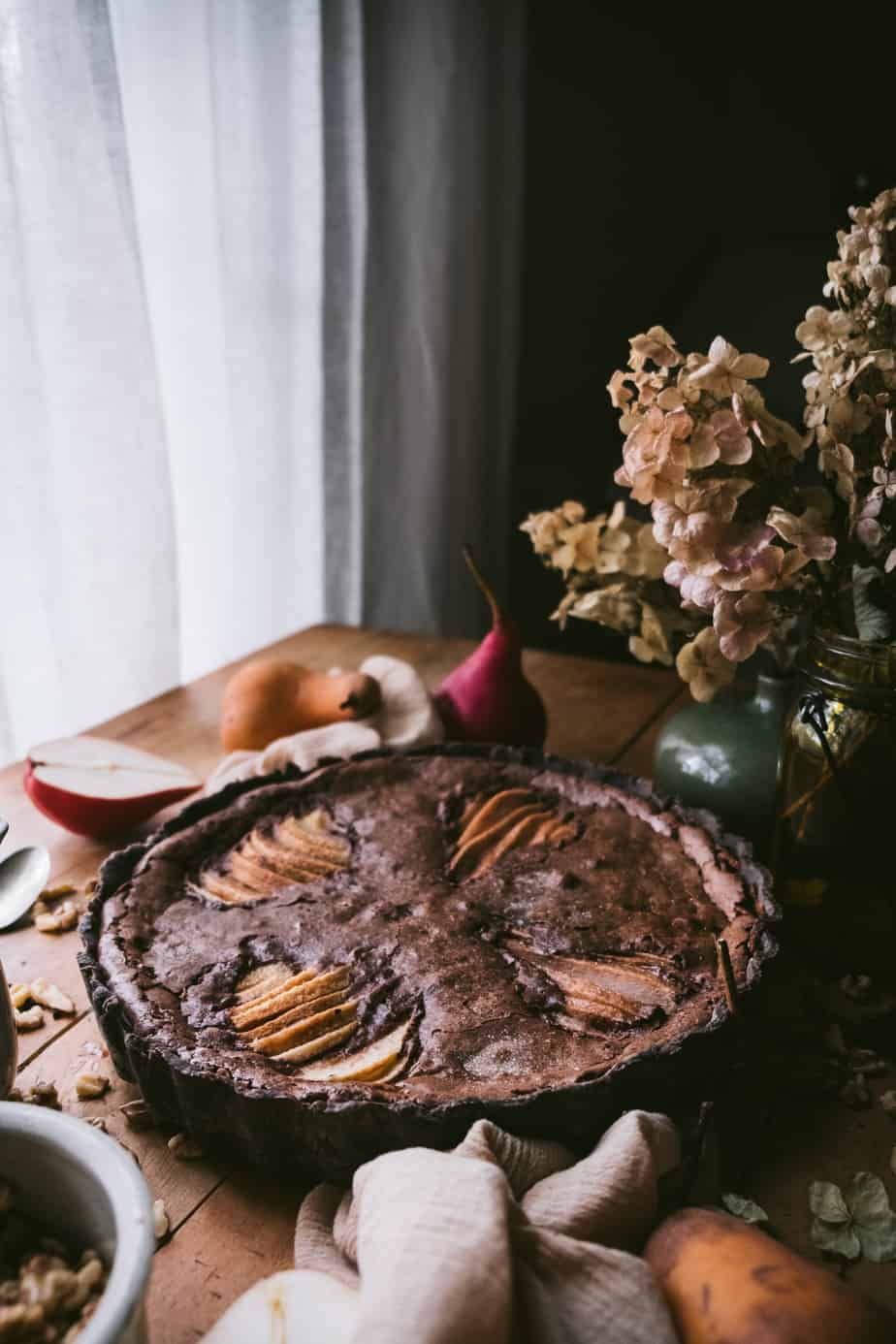 photo of chocolate tart with fruit and flowers next to window