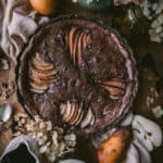 flatlay of chocolate walnut pear tart with fruit, flowers and props