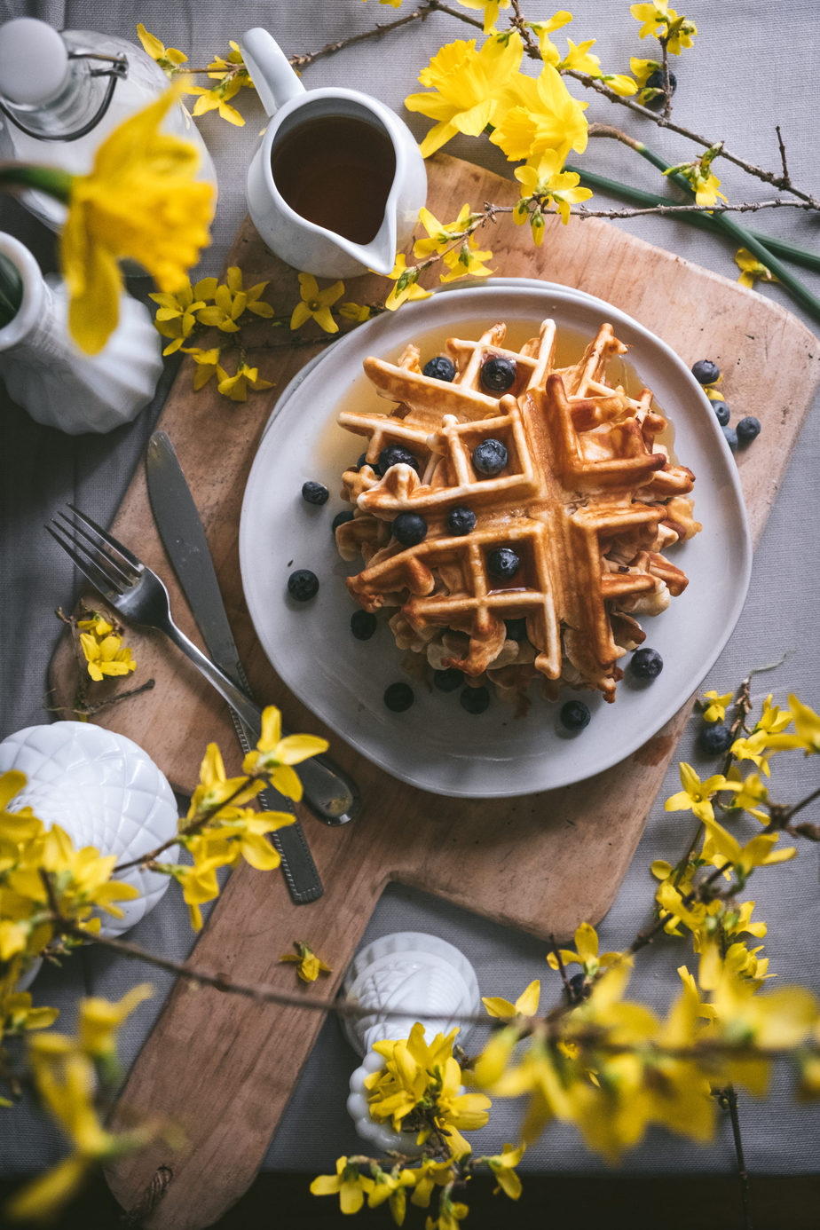 flatlay of breakfast scene with waffles, flowers and syrup