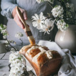 woman brushing hot cross milk bread with melted jam