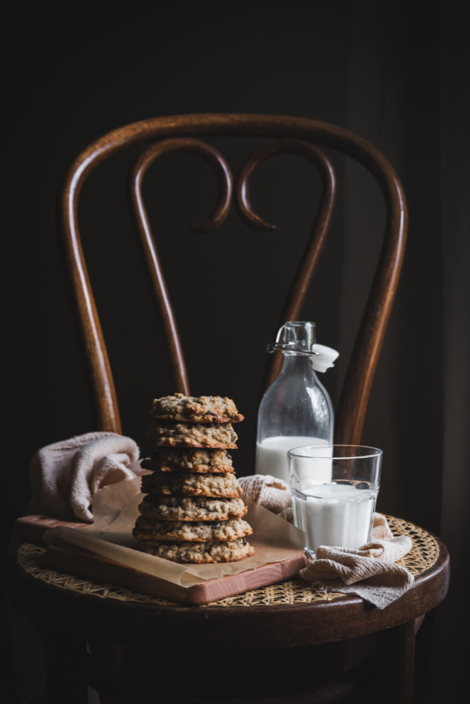 stack of oatmeal raisin cookies next to a glass of milk on a chair