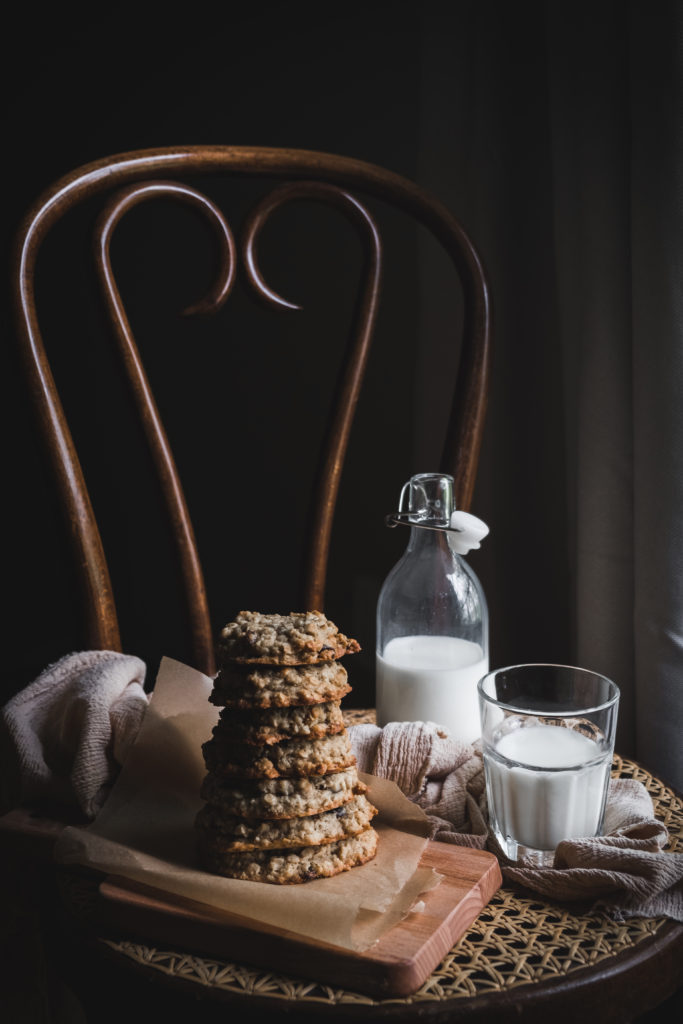 stack of oatmeal raisin cookies next to glass of milk on a chair